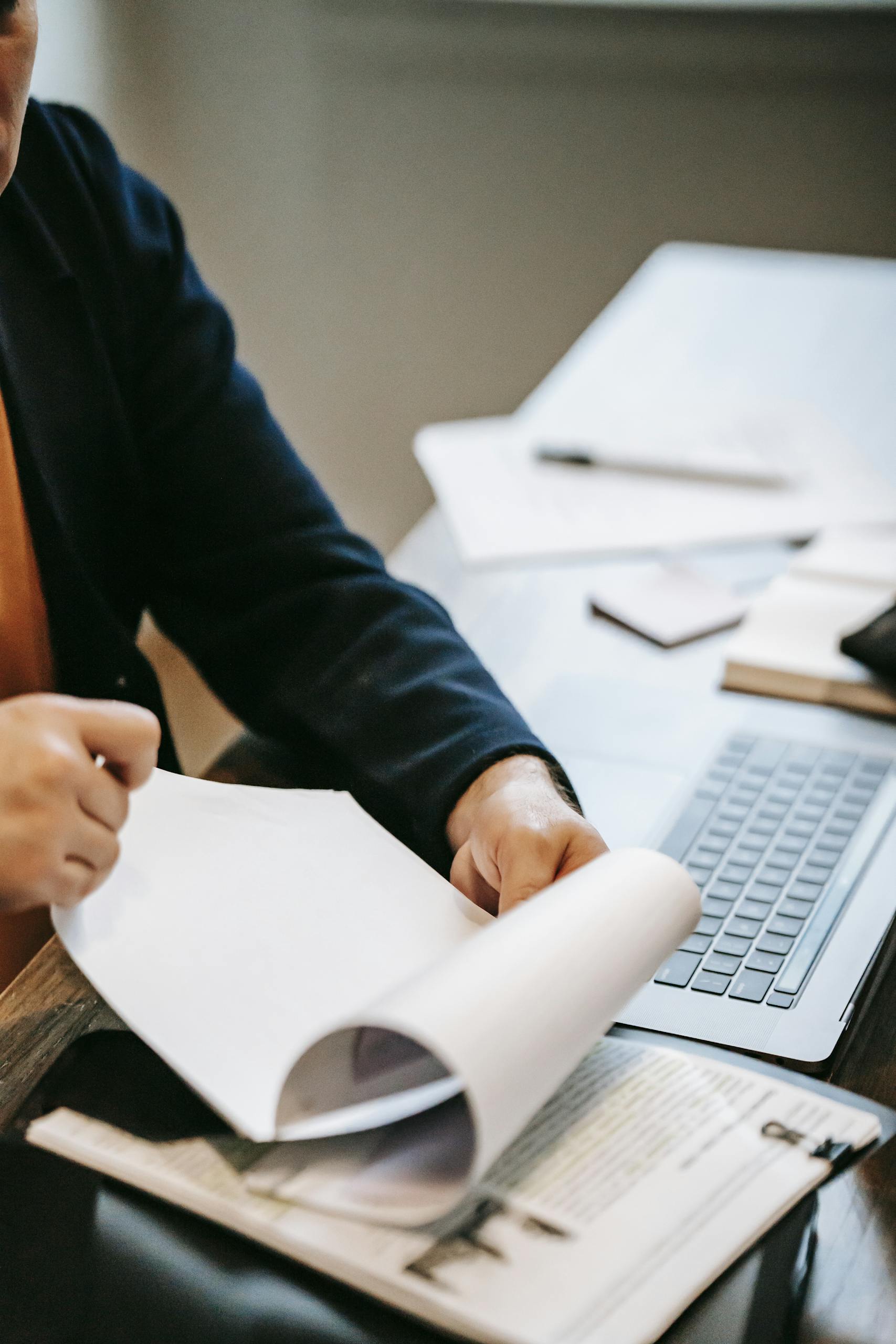 Person reviewing documents with laptop for work analysis.